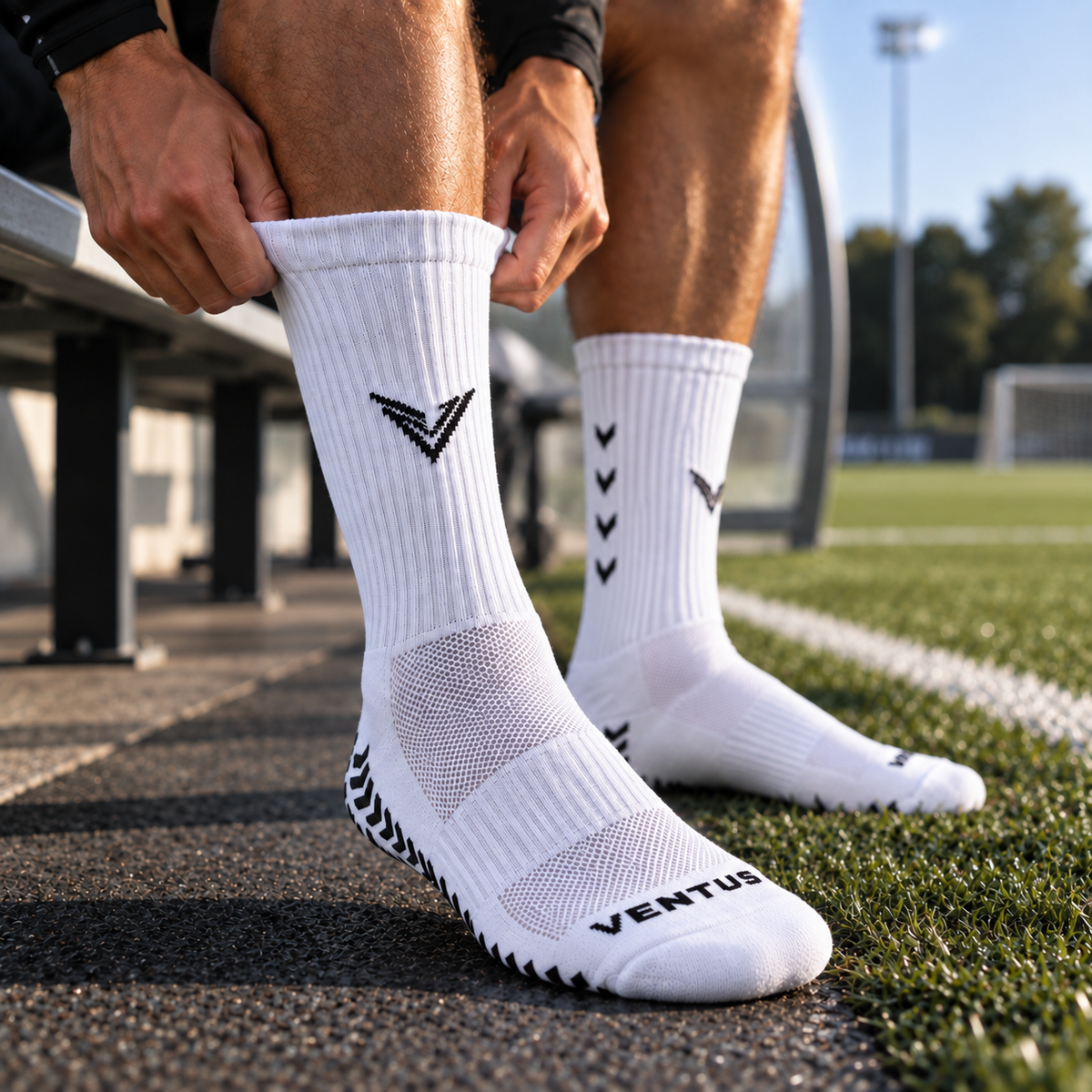 Player pulling on white Pro-Grip Socks at the side of a football pitch