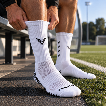 Player pulling on white Pro-Grip Socks at the side of a football pitch